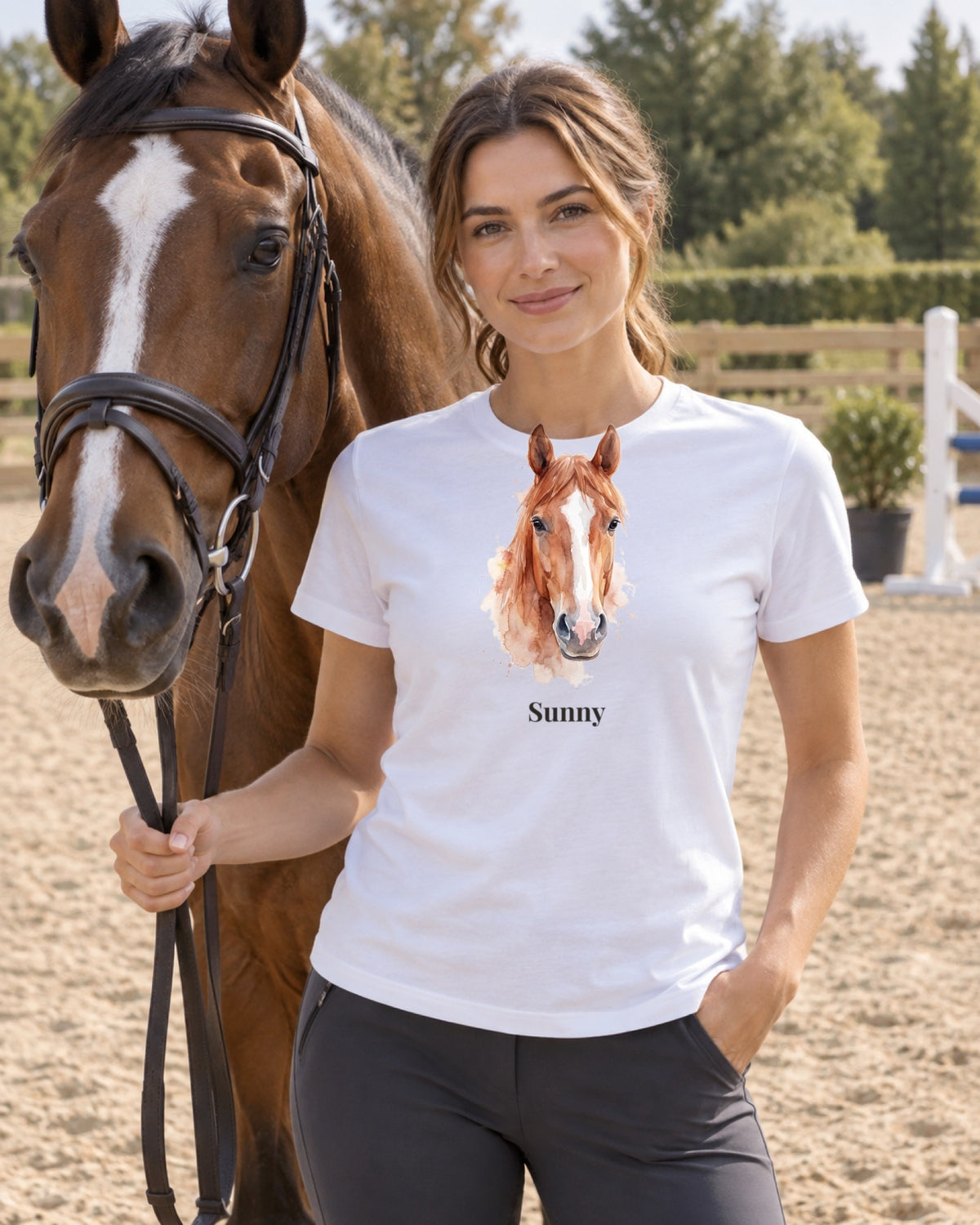 T-Shirt in Weiß mit Portrait von einem braunen Pferd im Stil Aquarell und dem Namen Sunny, getragen von einer Frau mit ihrem Pferd am Reitplatz