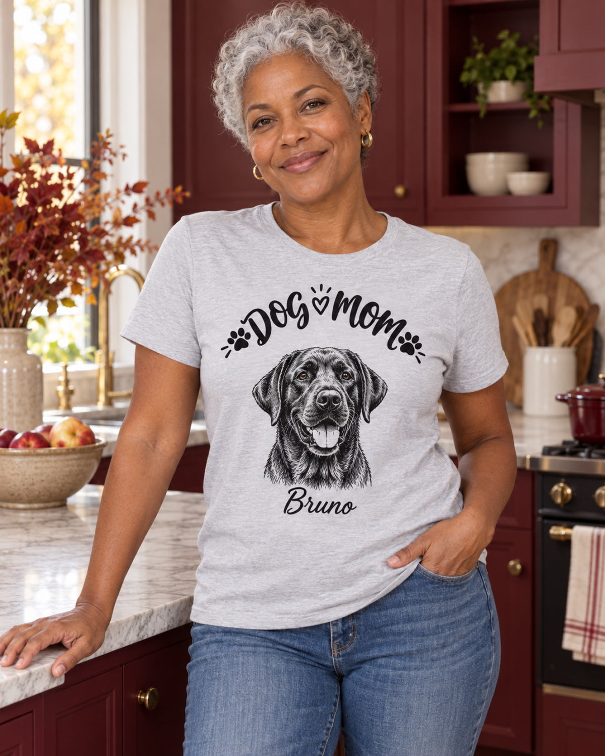 Frau im graumelierten Dog Mom T-Shirt mit Labrador Bruno als monochromer Linienzeichnung in einer burgunderroten Küche