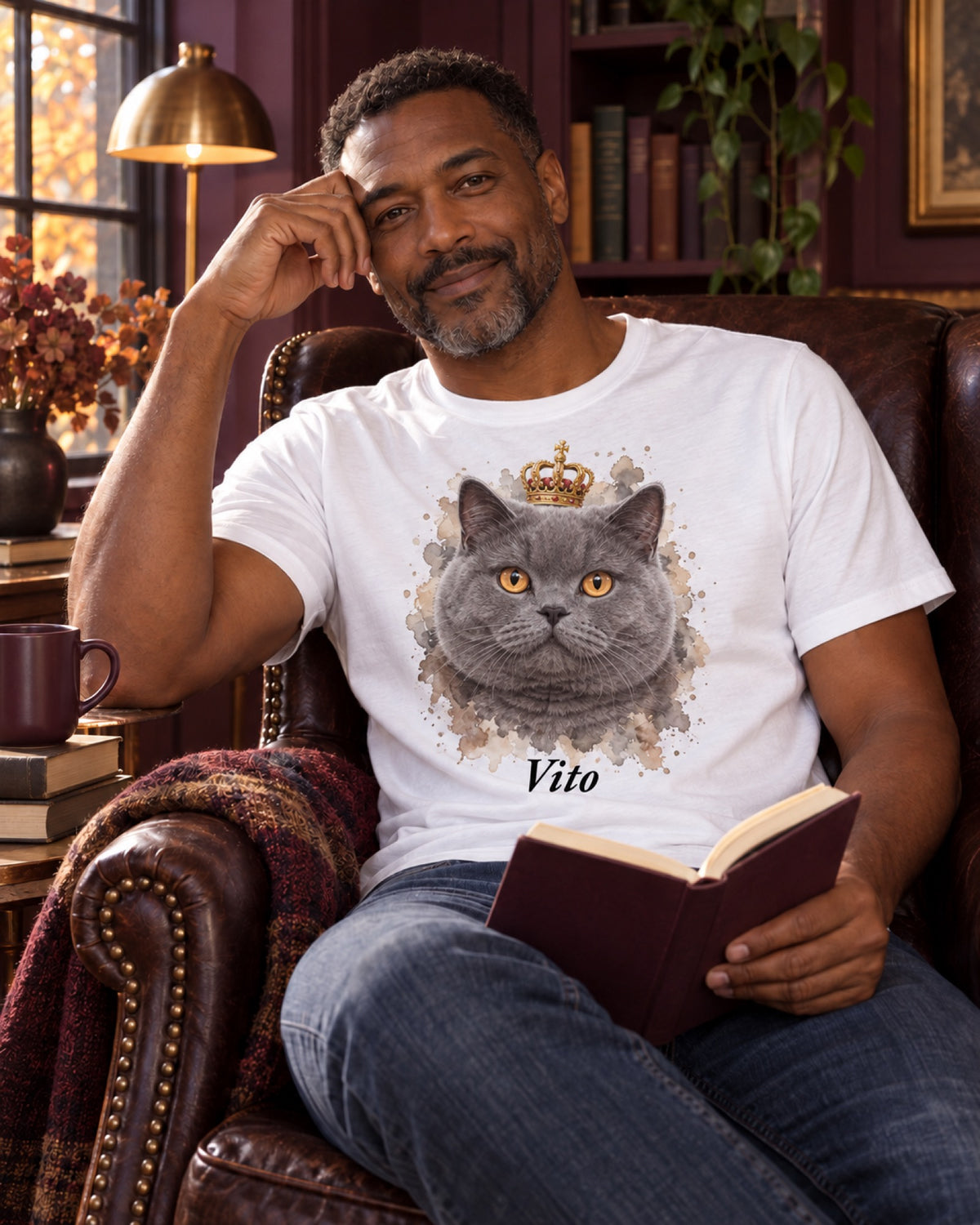 Mann im weißen T-Shirt mit grauer Britisch Kurzhaar Vito als Royalportrait im auberginefarbenen Herbstlesezimmer