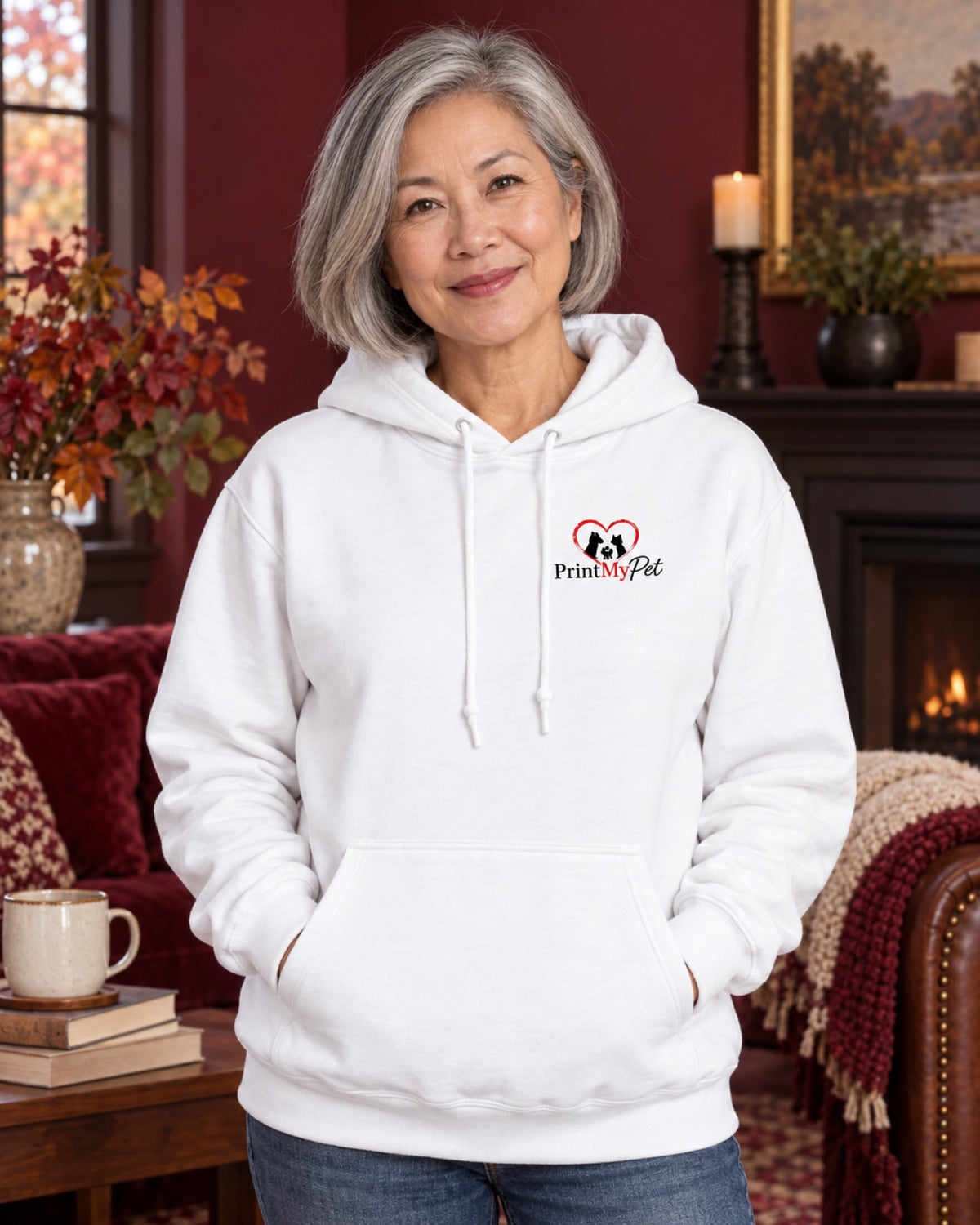 Frau im weißen PrintMyPet Edition Katze Hoodie mit kleinem Logo auf der linken Brust im burgunderroten Herbstwohnzimmer