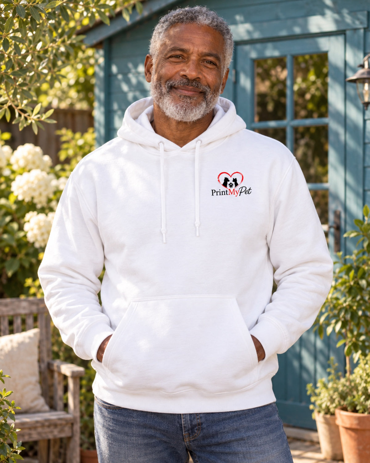 Mann im weißen PrintMyPet Edition Pferd Hoodie mit kleinem Logo auf der linken Brust vor einem tealblauen Sommergartenhaus
