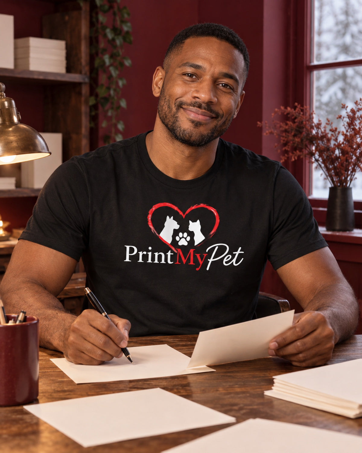 Mann im schwarzen PrintMyPet T-Shirt mit großem Logo auf der Brust im burgunderroten Atelier