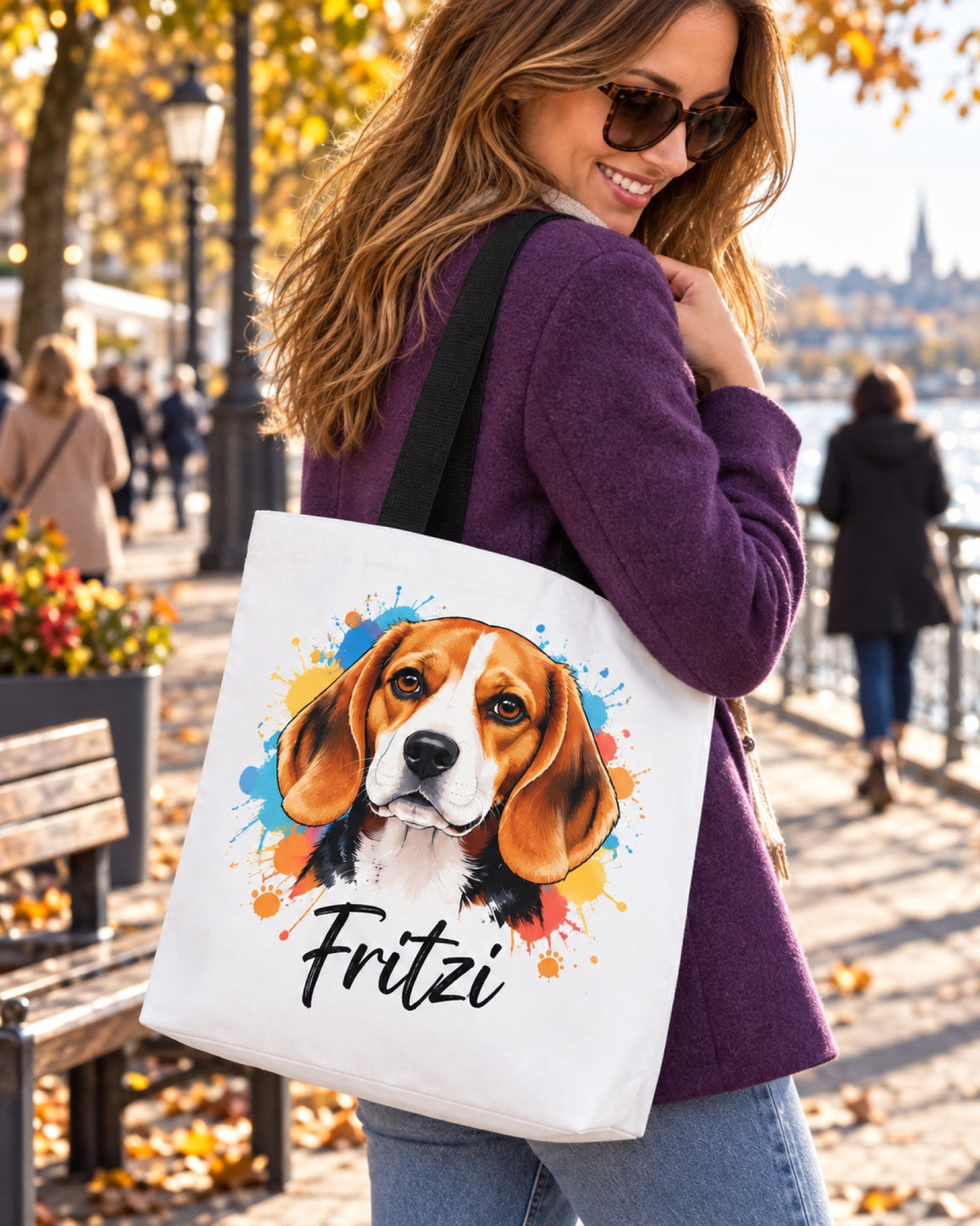 Weiße Stofftasche 39 × 39 cm mit schwarzen Henkeln, Beagle Portrait und Namen Fritzi über der Schulter einer Frau mit violetter Jacke auf einer herbstlichen Uferpromenade